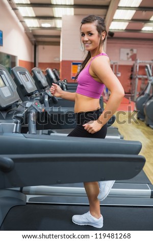 Woman running and training on a treadmill in a gym wearing black shorts and purple top smiling