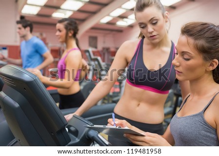 Female gym instructor and woman in the gym on the treadmill
