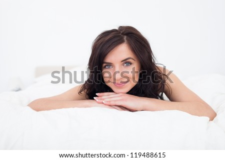 Brunette woman lying on her white duvet in her bedroom