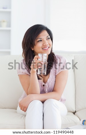 Woman sitting on a sofa and holding a glass of water in a living room