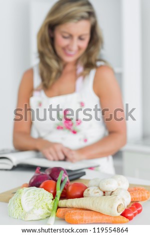 Woman reading recipe book beside vegetables on chopping board in the kitchen