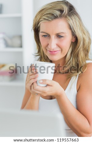Smiling woman holding mug looking at laptop