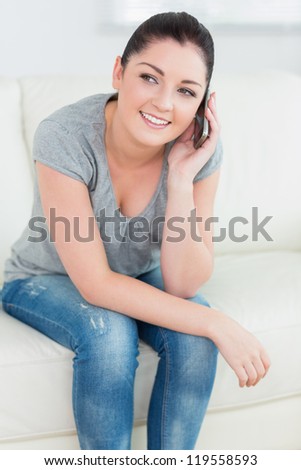 Telephoning woman sitting on the couch in a living room and smiling