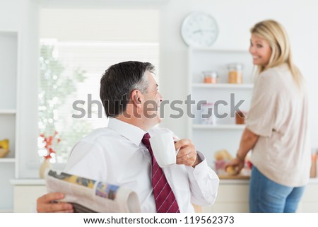 Couple laughing toghethe in kitchen before work with man holding mug and newpaper