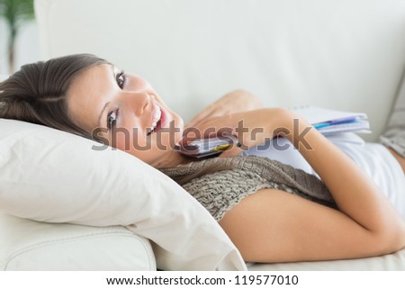 Smiling woman clutching notepad lying on the sofa at home