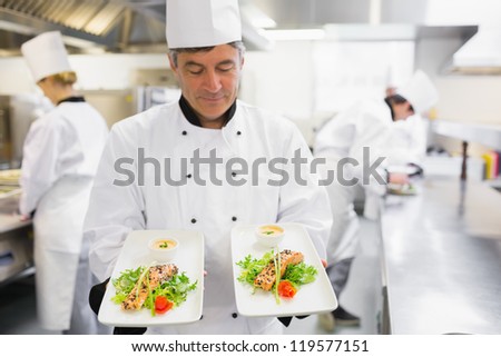 Chef admiring two salmon dishes in his hands in the kitchen
