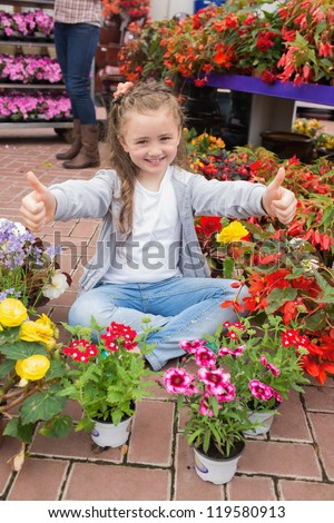 Little girl doing thumbs up sitting on the floor in garden centre
