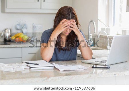 Stressed woman looking down at bills in kitchen