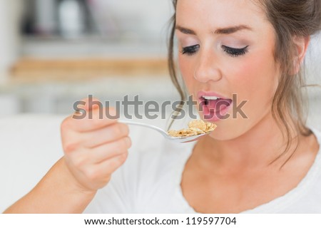 Girl lifting spoon of cereal to mouth on sofa