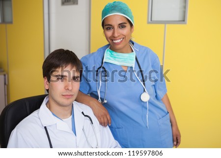 Happy doctor sitting in leather chair with nurse standing in yellow office