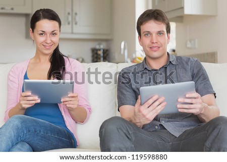 Friends sitting together on the couch while using tablet computers