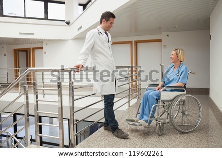 Doctor talks to nurse sitting in wheelchair in hospital corridor