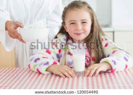 Happy little girl with glass of milk getting cereal from her mother at breakfast in kitchen
