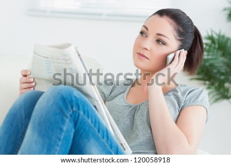 Woman sitting on the couch while reading the newspaper and using the phone
