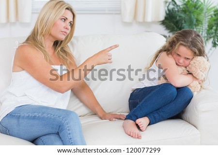 Angry mother scolding daughter clutchin teddy bear in living room