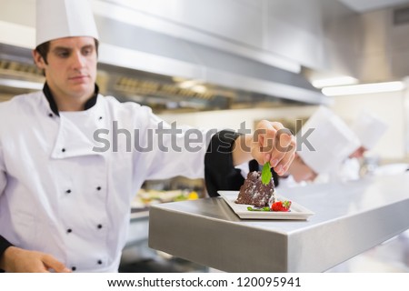 Chef garnishing his cake with a mint leaf in the kitchen