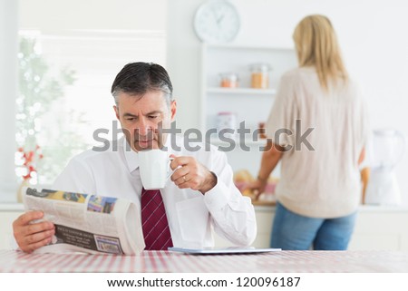 Man sitting at the kitchen table while reading a newspaper and holding a cup of coffee before work