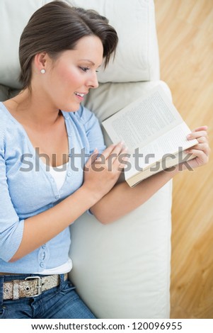 Smiling woman reading a novel lying on the sofa in the living room