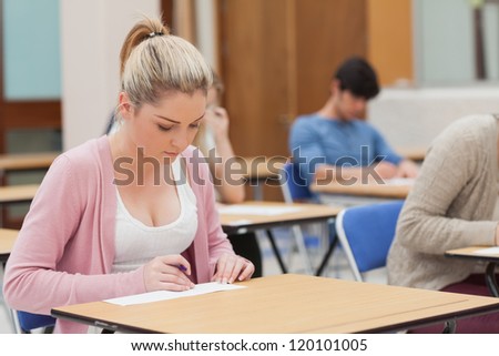 Blonde student writing note in classroom