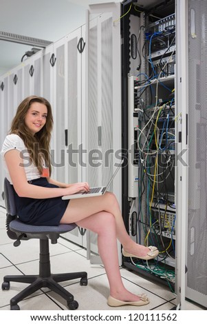 Happy woman with laptop working with servers in data center