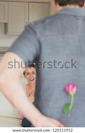 Man hiding flower behind his back for wife in living room