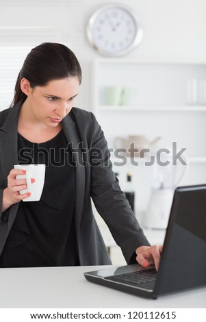 Woman looking at a laptop while holding a mug in a living room
