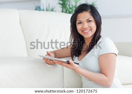 Smiling woman holding a tactile tablet in front of a sofa in a living room