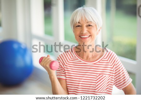 Portrait of happy senior woman exercising with dumbbell at home