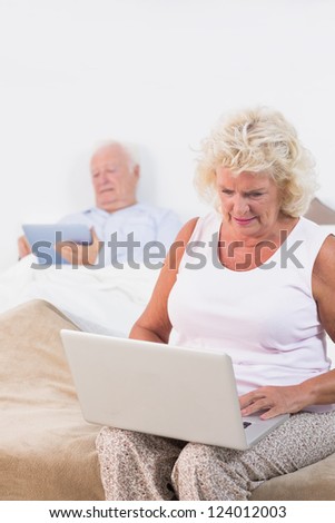 Old couple using a tablet and the laptop in the bedroom