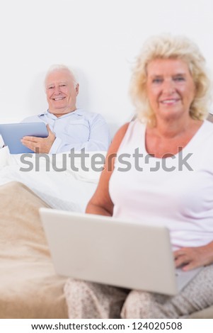 Happy old couple using a tablet and the laptop in the bedroom
