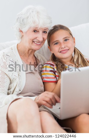 Happy girl using laptop with granny on the couch