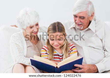Granddaughter reading book with grandparents on the couch