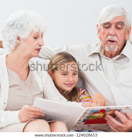 Little girl reading with grandparents on the couch