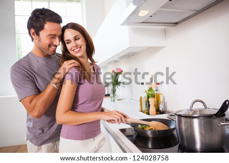Woman preparing food at the stove with partner behind her in kitchen