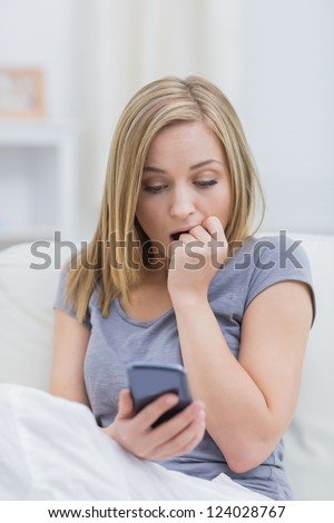 Casual shocked young woman looking at cellphone on sofa at home
