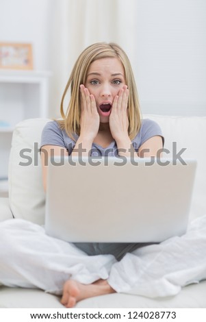 Portrait of shocked casual young woman with laptop on couch at home