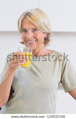 Smiling woman drinking orange juice in the kitchen