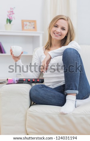 Portrait of young woman with coffee cup sitting on couch at home