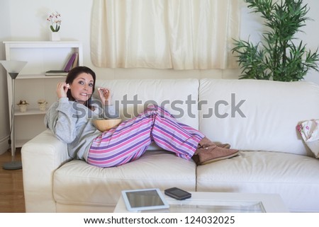 Young bored woman in nightwear sitting on couch and having popcorn at home