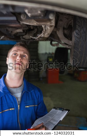 Young male mechanic with clipboard examining car in garage