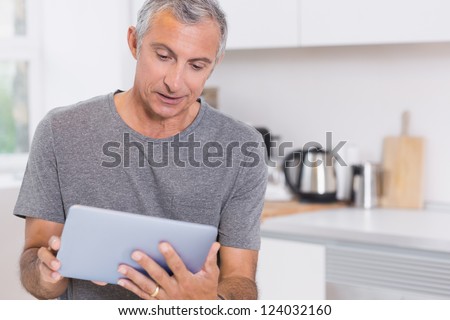 Mature man using his digital tablet in the kitchen