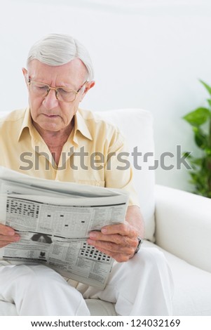 Focused elderly man reading the news in the living room