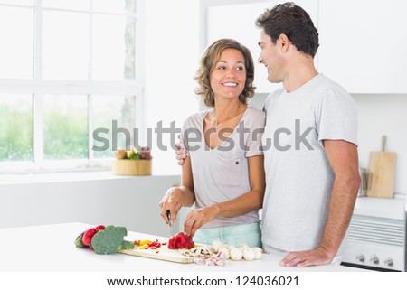 Husband embracing wife as she prepares vegetables in the kitchen