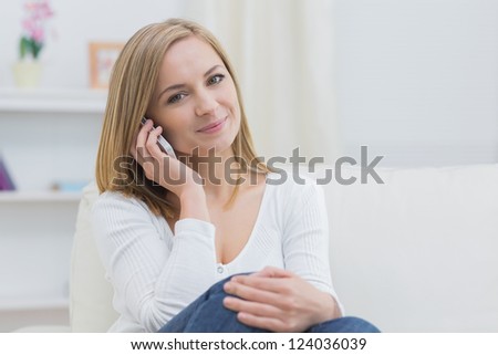 Portrait of casual young woman using mobile phone while sitting on couch at home