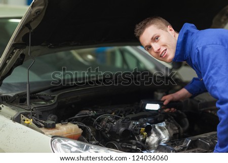 Portrait of confident repairman with flashlight examining car engine