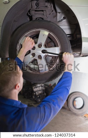 Male mechanic fixing car wheel in workshop