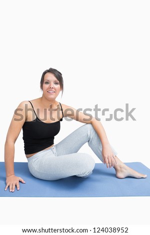 Portrait of young woman in sportswear sitting on yoga mat over white background