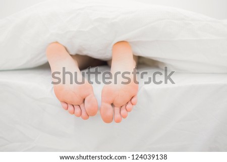 Woman\'s feet sticking out of blanket on bed at home