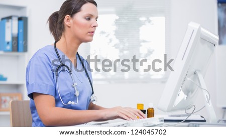 Side view of young female surgeon using computer at desk in clinic