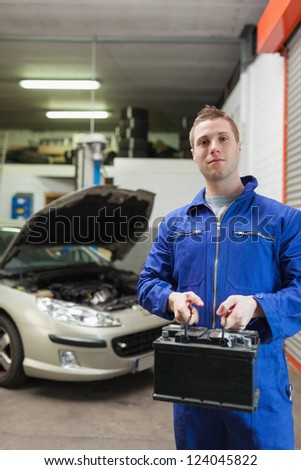 Portrait of confident auto mechanic with car battery in workshop